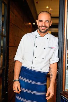 a man in a chef's uniform standing next to an open door with his hands on his hips