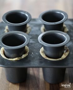 four black cups sitting in a muffin tin on top of a wooden table next to each other