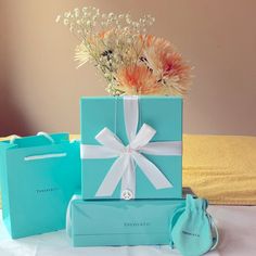 two blue boxes with white ribbons and flowers in them sitting on a bed next to each other