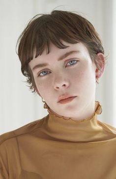 a woman with short hair and blue eyes wearing a brown shirt looking at the camera