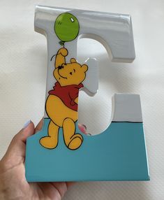 a hand holding a wooden letter shaped like a winnie the pooh with a balloon