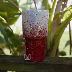 a red and white cup sitting on top of a wooden table next to a plant