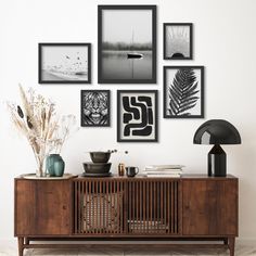 there are many framed pictures on the wall above this sideboard, including plants and vases