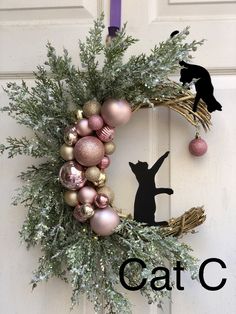 a christmas wreath with ornaments and a cat silhouette hanging on the front door to welcome guests