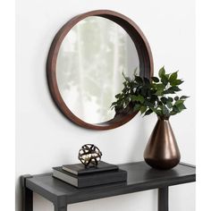 a round mirror sitting on top of a table next to a vase with a plant