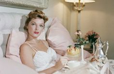 a woman laying in bed next to a vase with flowers and a cake on it