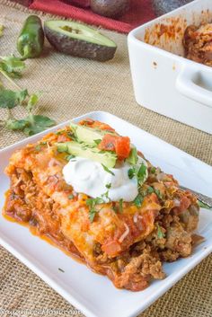 an enchilada casserole with sour cream on top is sitting on a white plate