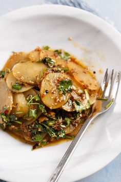 a white plate topped with potatoes covered in gravy next to a knife and fork