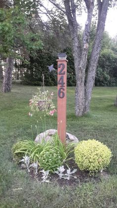 a wooden sign sitting in the middle of a lush green field next to a tree