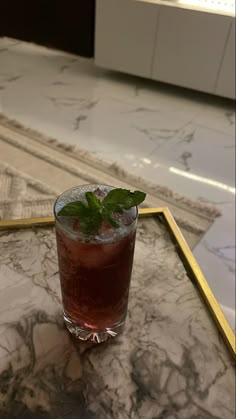 a drink sitting on top of a marble counter next to a gold tray with a green leaf