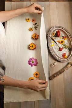 a woman sitting at a table with flowers on her lap and cutting up petals from the paper