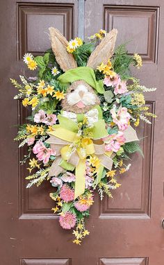 a wreath with flowers and a bunny on the front door is hanging on a brown door