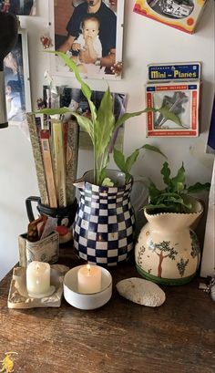 a wooden table topped with vases filled with plants and candles next to pictures on the wall