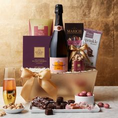 a bottle of wine, chocolates and champagne in a basket with two glasses on the table