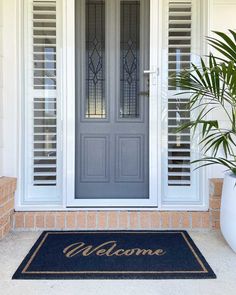 a welcome mat with the words welcome on it in front of a white door and potted plant