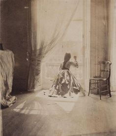 an old photo of a woman sitting in front of a window looking out the window