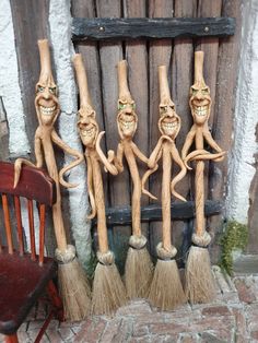 three wooden statues with faces and hands holding brooms in front of an old door