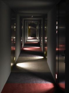 an empty hallway with red carpet and light coming in from the doors on either side