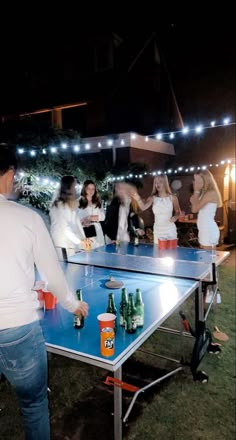 a group of people playing ping pong in the yard at night with beer cans