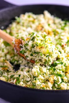 a pan filled with rice and broccoli being stirred by a wooden spoon