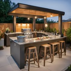 an outdoor kitchen with bar stools next to it and lights hanging from the ceiling