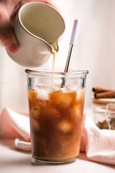 someone is pouring tea into a glass with ice and cinnamon on the table next to it