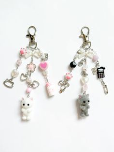 two key chains with charms attached to them on a white surface, one has a teddy bear and the other is a cat