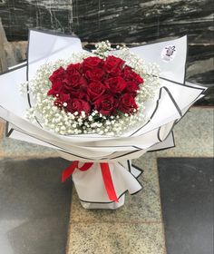 a bouquet of red roses and baby's breath wrapped in white paper on a marble surface