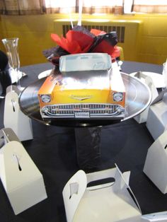 an old car is sitting on top of a round table with white chairs and napkins