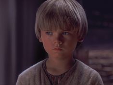 a young boy with blonde hair stares into the distance