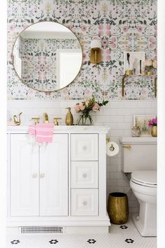 a white bathroom with floral wallpaper and gold accents on the mirror above the sink