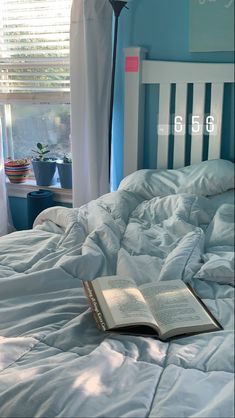 an open book laying on top of a bed in a room with blue walls and curtains