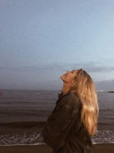 a woman standing on top of a beach next to the ocean with a kite flying in the air