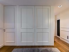 an empty room with white doors and wood floors, along with a rug on the floor