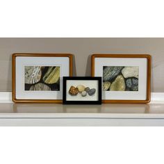 two framed pictures sitting on top of a mantle next to rocks and pebbles in front of them