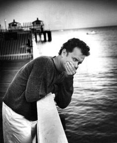 black and white photograph of a man leaning on a railing looking at the water with his hands to his face