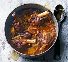 a pot filled with meat and carrots on top of a marble countertop next to a knife