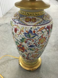 an ornate vase is sitting on the floor next to a light fixture with a cord in front of it