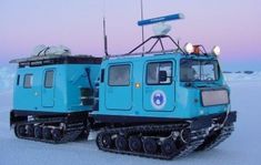 two snowmobiles sitting in the middle of an open field covered in snow at dusk