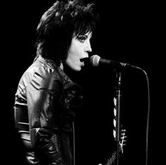 a black and white photo of a woman singing into a microphone while holding a guitar