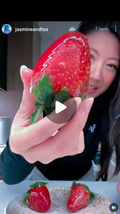 a woman holding up a strawberry on top of a plate