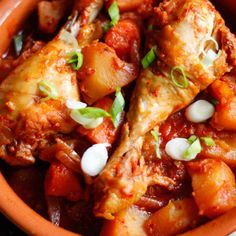 a bowl filled with meat and potatoes covered in tomato sauce, garnished with scallions