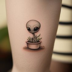 an alien tattoo on the leg of a woman's leg, with a potted plant in it