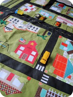 a child's quilted play mat with cars and houses on the road in green