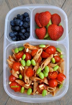 a plastic container filled with pasta, berries and blueberries on top of a wooden table