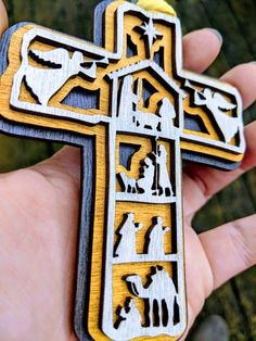 a hand holding a wooden cross with images of people and animals on it in the center