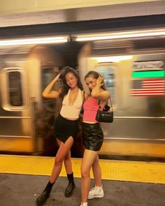 two young women standing next to each other in front of a train at a station