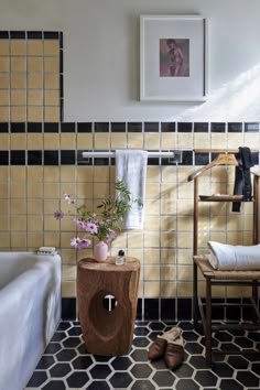 a bathroom with yellow and black tiles on the walls, a wooden stool next to a white bathtub