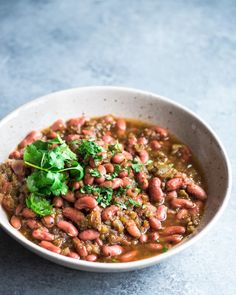 a white bowl filled with beans and cilantro on top of a blue surface