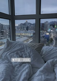 an unmade bed in front of large windows overlooking the city